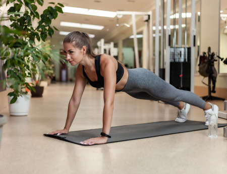 Slim fit woman in sportswear getting ready doing push-ups from the floor in the gym. Healthy...