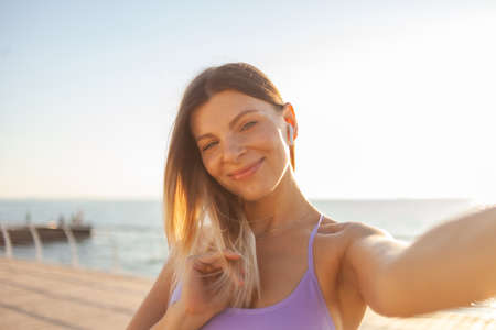 Selfie portrait of a young blonde woman dressed in sportswear on the beach at sunrise