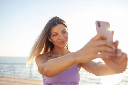 Selfie portrait of a young blonde woman dressed in sportswear on the beach at sunriseの写真素材