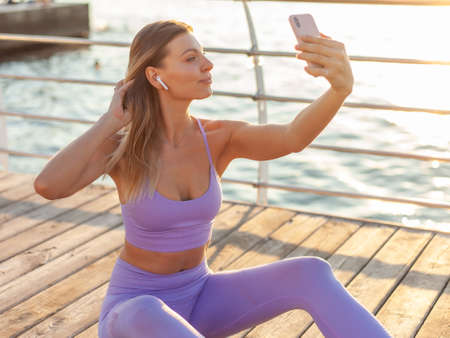 Morning workout. Young woman in sportwear with earphones doing selfie portrait on smartphone on the...