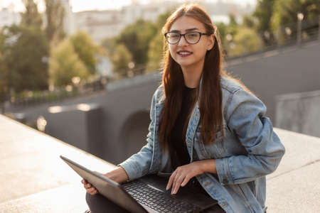 Young modern woman student in a denim jacket sitting with laptop. Distance learning. Modern youth...
