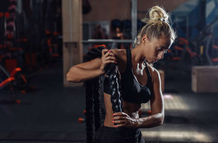 Young sport woman in sportswear is training with battle rope on her shoulders in the gym. Functional training. Healthy lifestyle conceptの写真素材