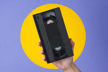 Female hand holding video cassette on purple background with yellow circleの写真素材