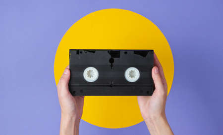 Female hand holding video cassette on purple background with yellow circleの写真素材
