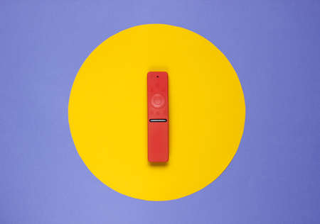 Modern tv remote in a case on colored paper background with yellow circle in the middle. Top view....