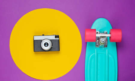 Cruiser board and retro film camera on purple background with a yellow circle. Summer fun. Studio fashion shot. 80s, pop culture. Top view.の写真素材