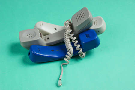 Three office phone tubes wrapped in cable on blue studio background. Call center, hotline concept
