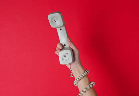 Female hand wrapped in cable holds phone tube against red background. Port art. Creative minimalism. Top viewの写真素材