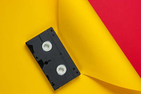 Video cassette tape on red yellow creative studio background. Minimalistic fashion shot.