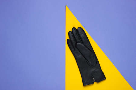 Leather gloves on purple paper background with yellow geometric shapes. Minimalistic fashion still...