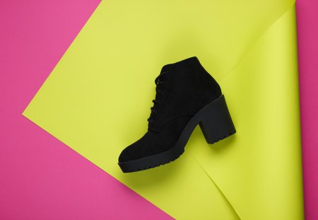 Black suede boot on neon folded paper background. Minimalistic fashion still life. Flat lay. Top viewの写真素材