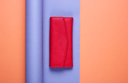 Red leather wallet on wrapped paper background. Color trend, minimalistic fashion still life. Top...