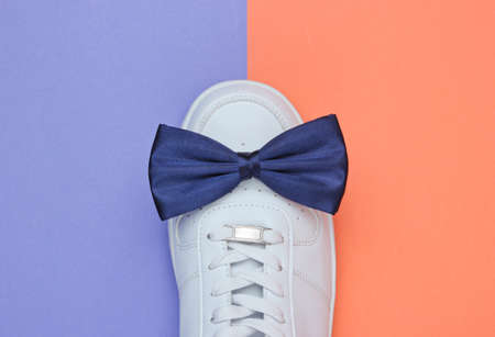 Stylish white sneaker with a bow-tie on a two-color paper background. Minimalistic fashion concept. Top viewの写真素材