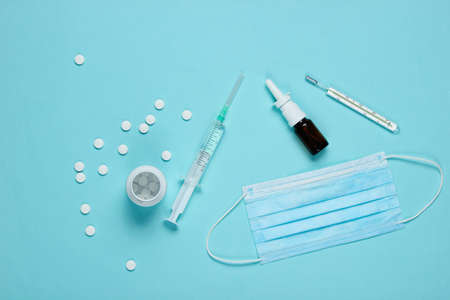 Medical still life on a blue background. Syringe, medical mask, thermometer, pills, nasal spray....
