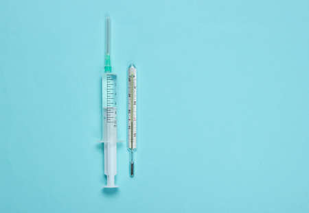 Medical still life on a blue background. Syringe, thermometer. Minimalism