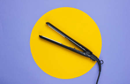 Hair straightener on a purple background with yellow circle in the middle. Top view. Minimalistic beauty and fashion conceptの写真素材