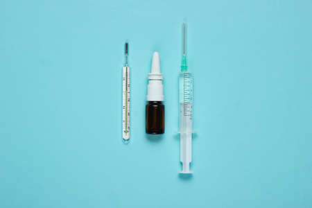 Medical still life on blue background. Syringe, thermometer, nasal spray. Minimalism