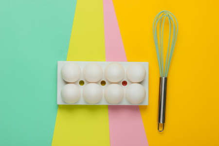 Tray with white chicken eggs and whisk on colored background. Minimalistic food concept. Top viewの写真素材