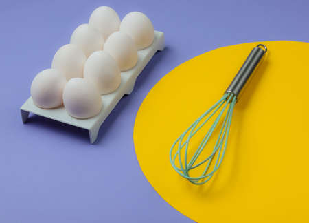 Tray with white chicken eggs and whisk on blue background. Minimalistic food concept.の写真素材