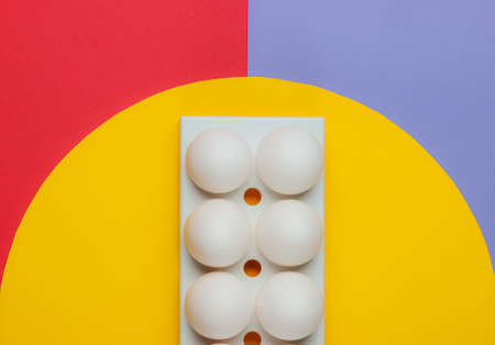 A tray with white chicken eggs on colored background with yellow circle in the middle. Minimalistic...