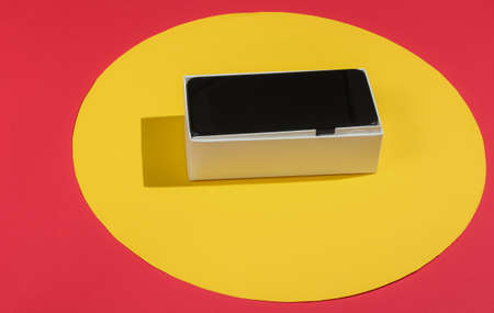 New modern smartphone in box on red background with yellow circle in the middle. Minimalistic fashion concept, giftの写真素材