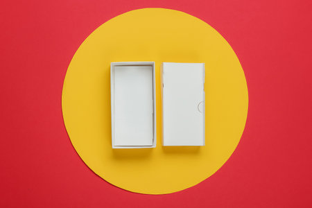 Empty cardboard box from a modern smartphone on red background with yellow circle in the middle. Top...