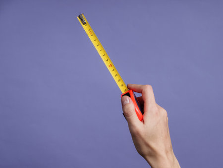 Female hands take measurements with industrial tape measure on purple backgroundの写真素材