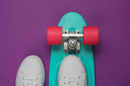 Stylish white sneakers with cruiser board on purple background. Summertime fun. Studio shot, top view.の写真素材