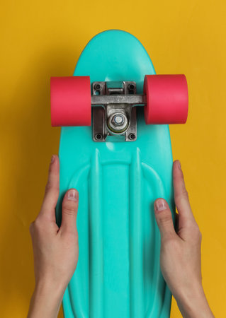 Female hands hold cruiser board on yellow background. Top viewの写真素材