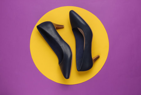Classic women's high heel shoes on purple background with yellow circle in the middle. Stylish shoes. Minimalistic fashion still life. Top viewの写真素材