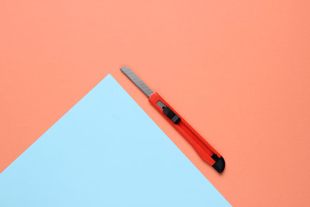 Stationery knife for cutting paper on colored background. Top viewの写真素材