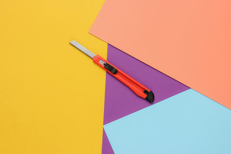 Stationery knife for cutting paper on colored background. Top viewの写真素材