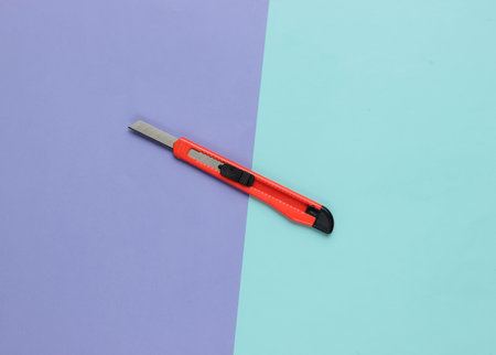 Stationery knife for cutting paper on colored background. Top viewの写真素材