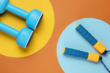 Minimalistic sport still life. Skipping rope and dumbbells on colored background. Top viewの写真素材