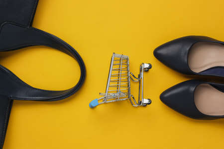 Minimalistic fashion and shopping concept. Leather high heel shoes, shopping trolley, bag on yellow background. Top viewの写真素材