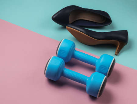 Leddy's sport. Women's high heel shoes with dumbbells on pastel background. Fitness and fashion...