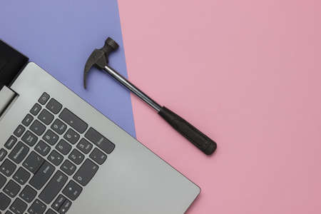 Service center, laptop repair. Laptop and hammer on pink purple background. Top viewの写真素材