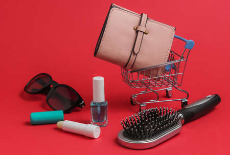 Minimalistic shopping concept. Mini shopping trolley with female accessories on red backgroundの写真素材