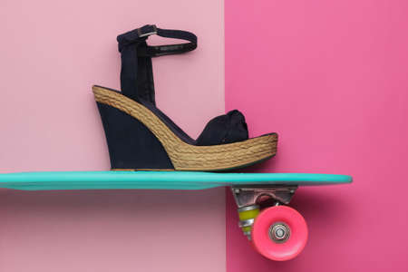 Summer fun. Women's sandals on platform with cruiser board on pink studio background. Fashion shot,...