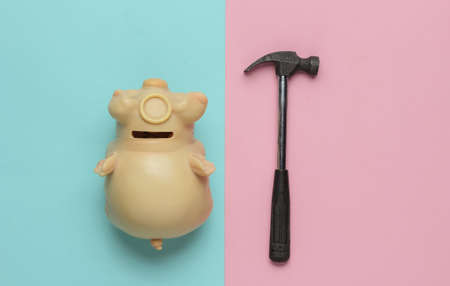 Minimalism fashion concept. Piggy bank with hammer on pink-blue background. Top view