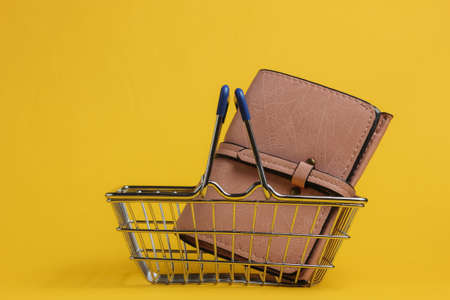 Minimalistic shopping concept. Mini shopping basket with wallet on yellow backgroundの写真素材