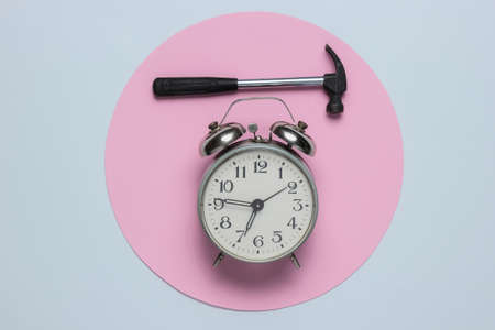 Alarm clock with hammer on white background with pink circle. Top view. Minimalism