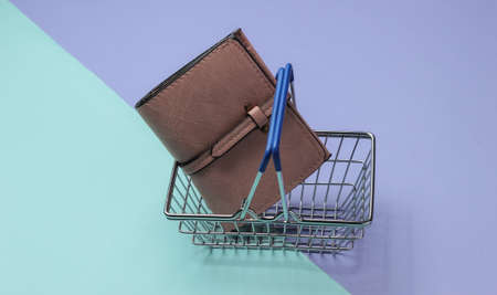 Minimalistic shopping concept. Mini shopping basket and leather wallet on purple blue background.の写真素材