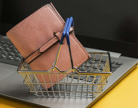 Online shopping concept. Laptop and mini shopping basket with basket on yellow background