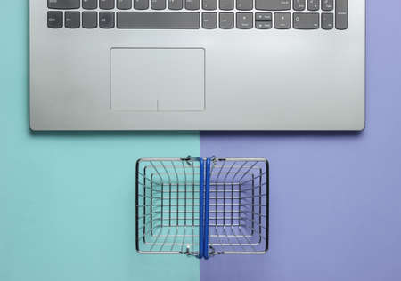 Online shopping concept. Laptop and mini shopping basket on purple-blue pastel background. Top viewの写真素材