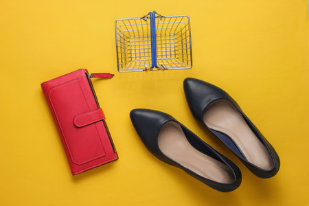 Shopping concept. Fashion studio shot. Women's high-heeled shoes, shopping basket, wallet on yellow...