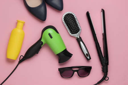 Women's accessories. Hair care. Beauty studio shot. Hair dryer, straighteners, bottle shampoo, comb, sunglasses, high heel shoes on pink pastel background.の写真素材