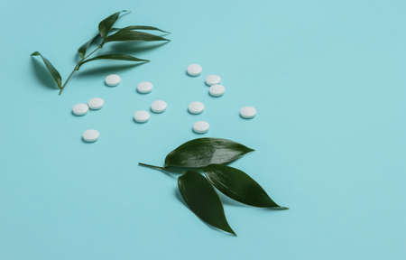 Herbal pills. White pills with green leaves on a blue pastel background. Minimalistic medicine still lifeの写真素材