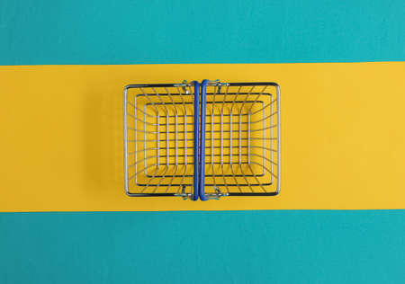 Minimalistic shopping concept. Shopping basket on blue-yellow background.の写真素材