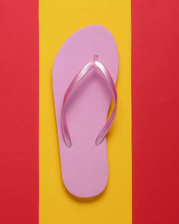 Pink flip flops on a yellow-red background. Top view. Minimalism.